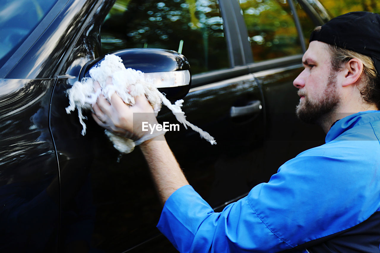 Side view of young man with cleaning cloth in hand washing his car 