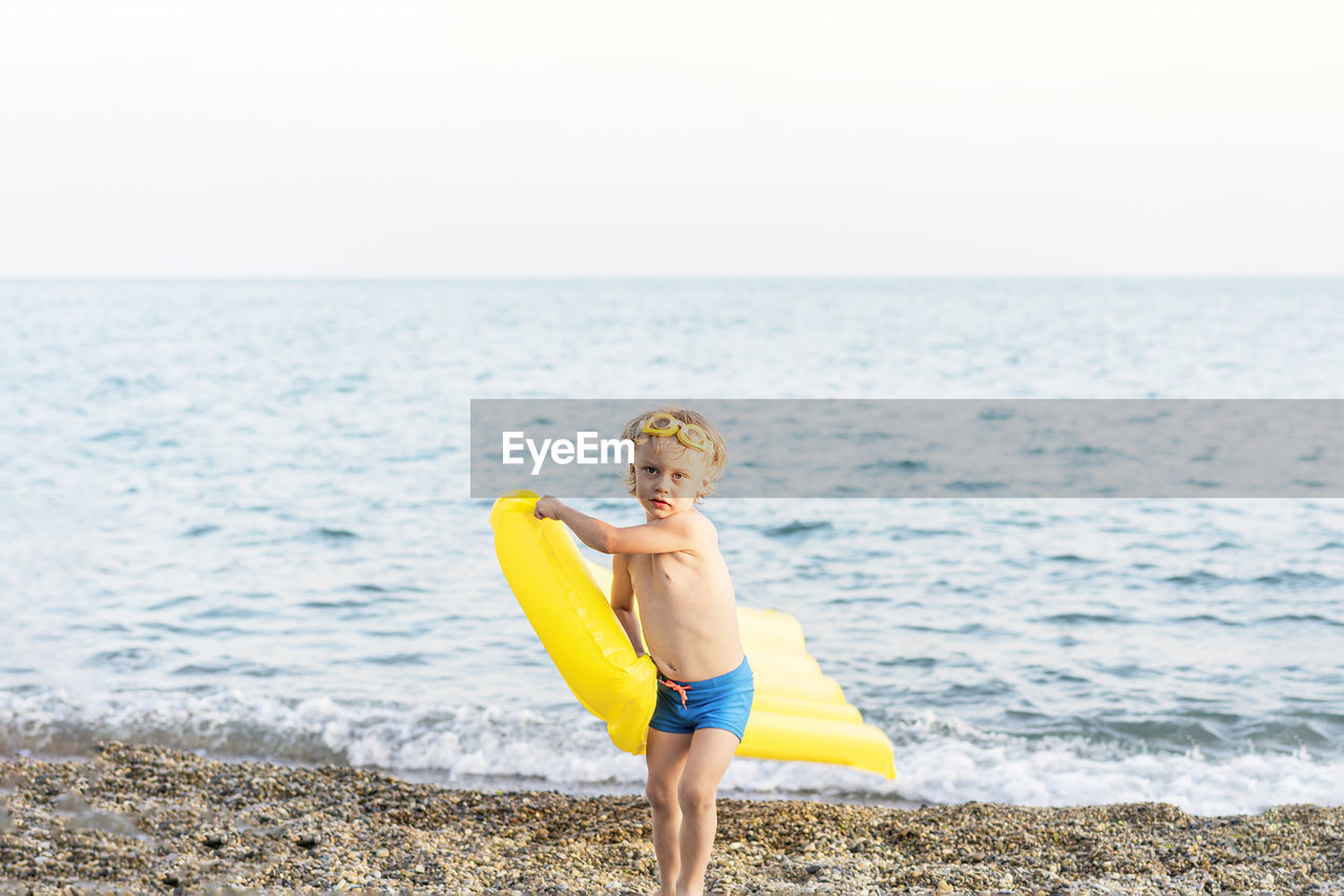 Cute funny little boy playing with yellow swimming mattress at sea shore. summer beach vacation