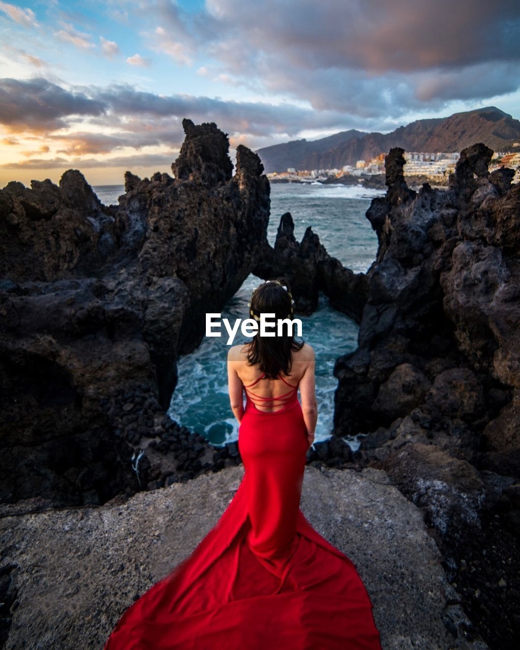 Rear view of woman wearing red dress while standing on cliff