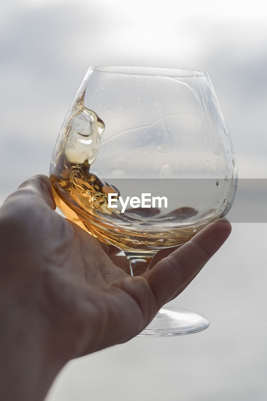 Cropped image of hand holding brandy snifter against sea