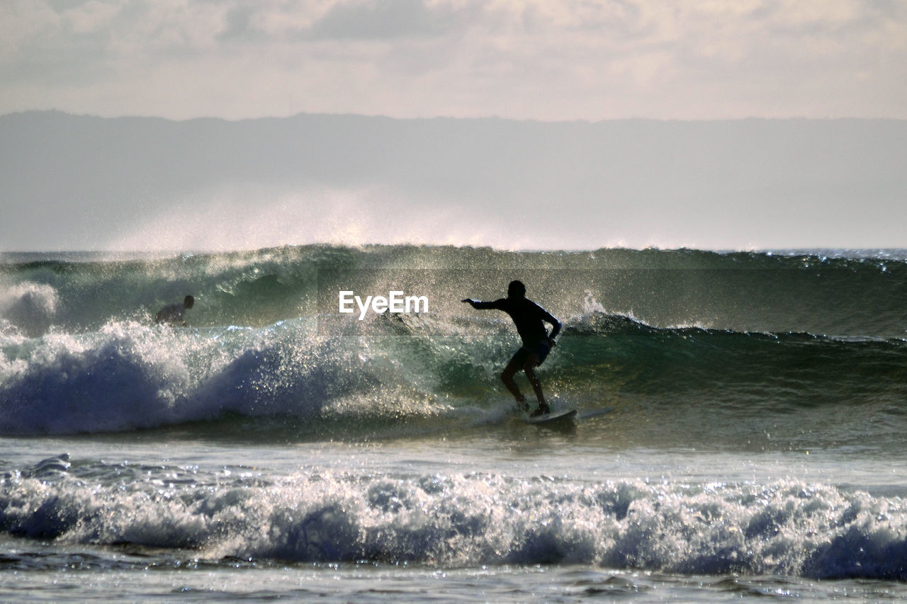 Silhouette man surfing in sea against sky