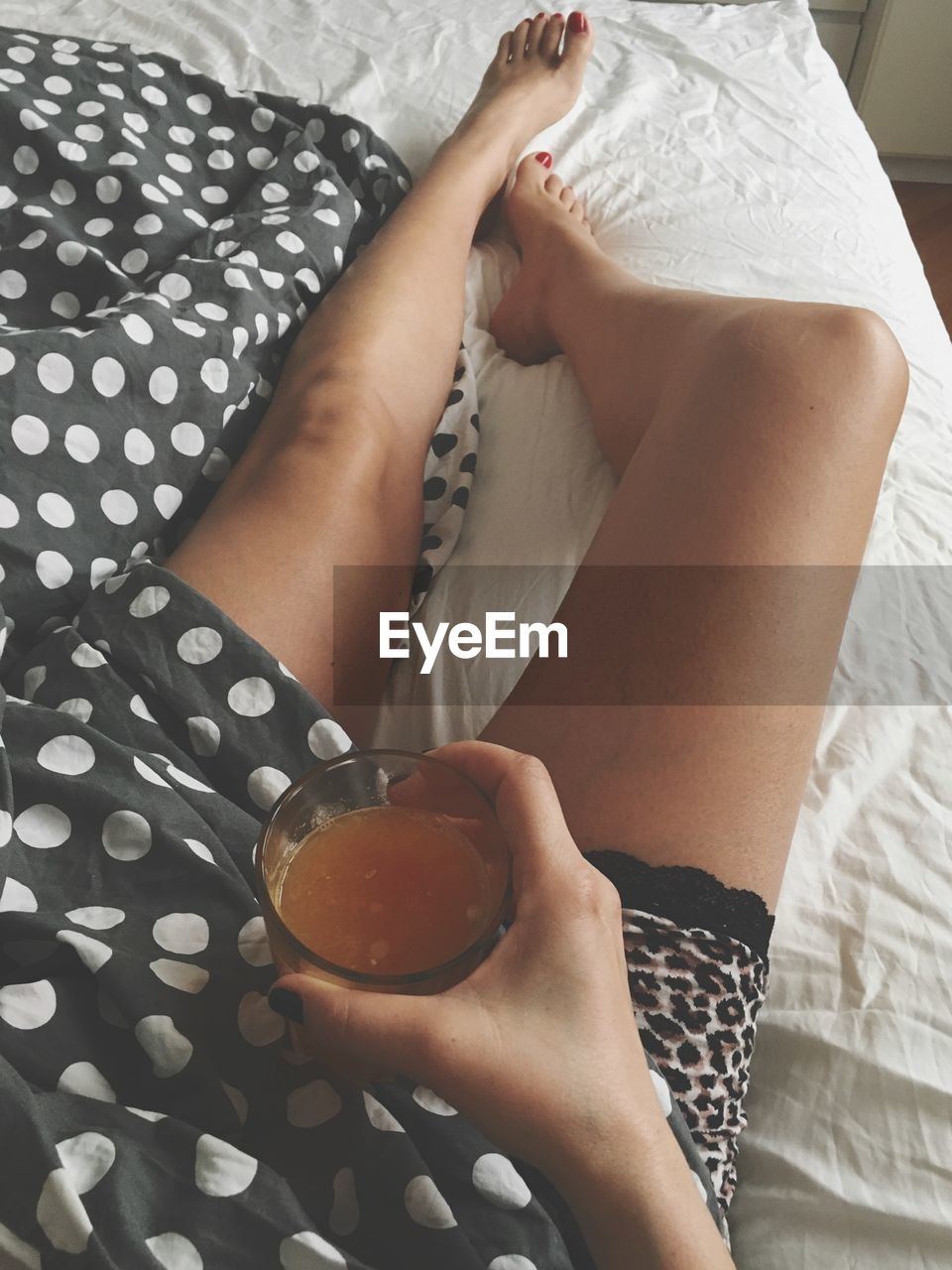 Low section of woman holding drink while lying on bed