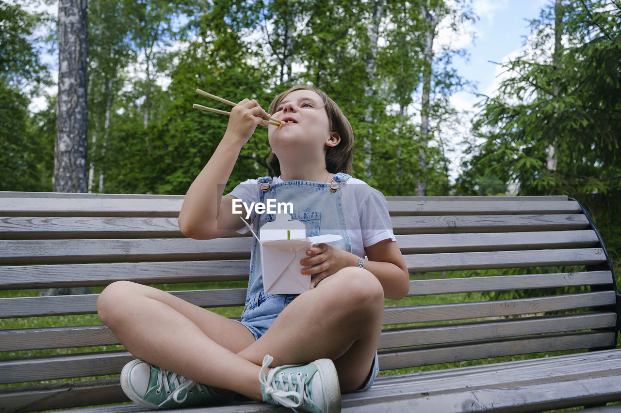 Teenage girl on a walk on a summer day in the park has lunch with noodles wok