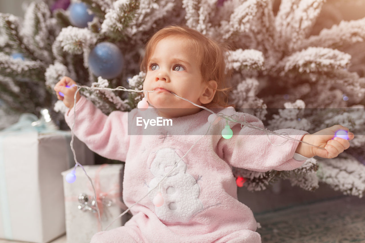 Cute girl eating wire of christmas lights at home