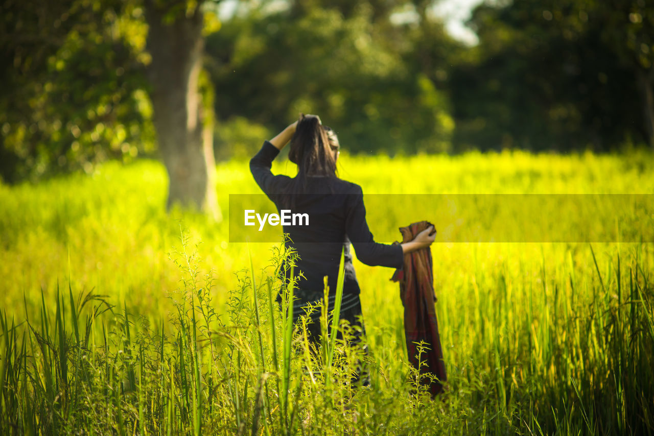 Rear view of young woman standing amidst grassy field