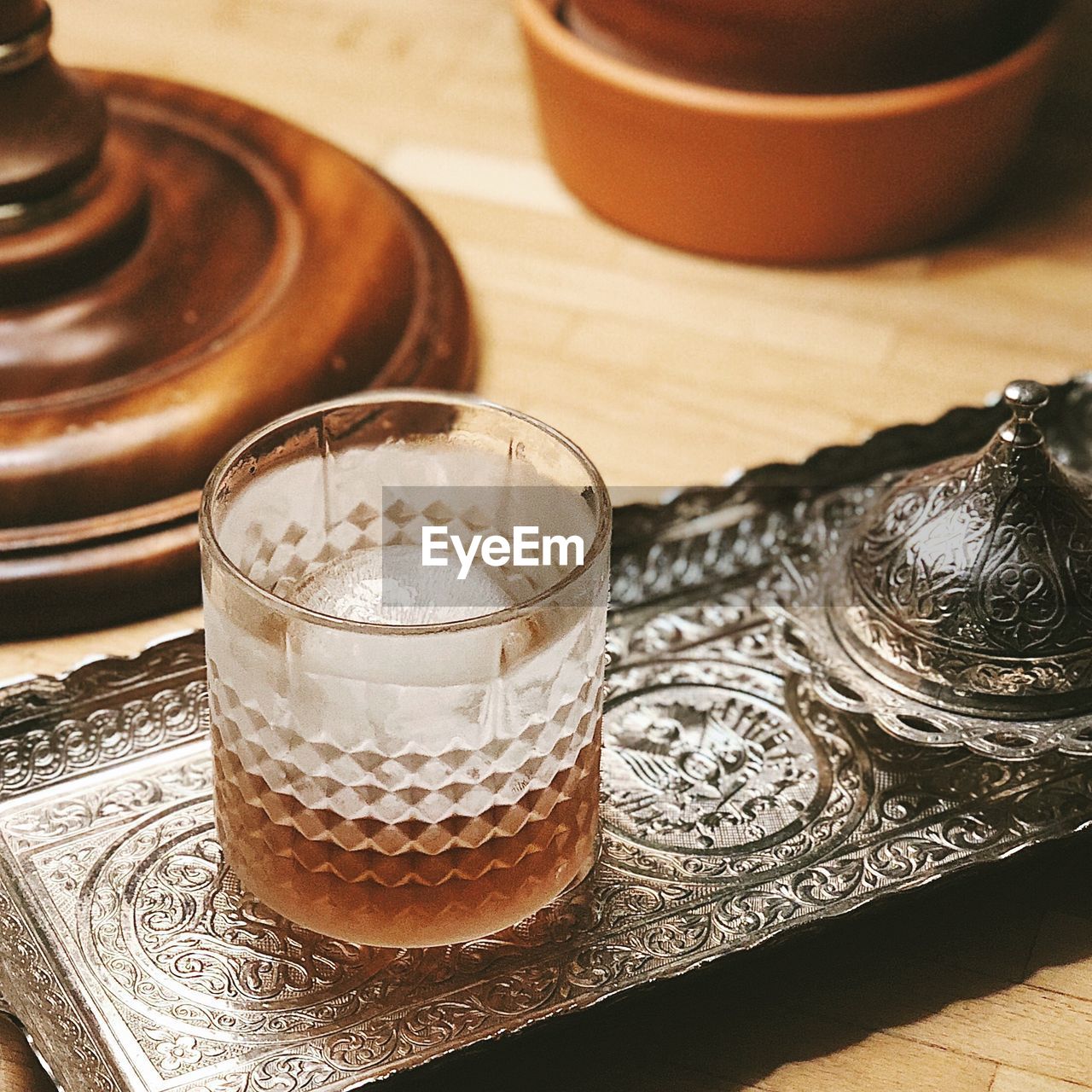 High angle view of brown clear drink in glass on oriental metal tray