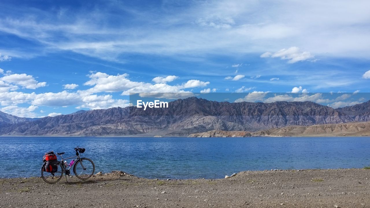 PEOPLE RIDING BICYCLE BY WATER AGAINST SKY