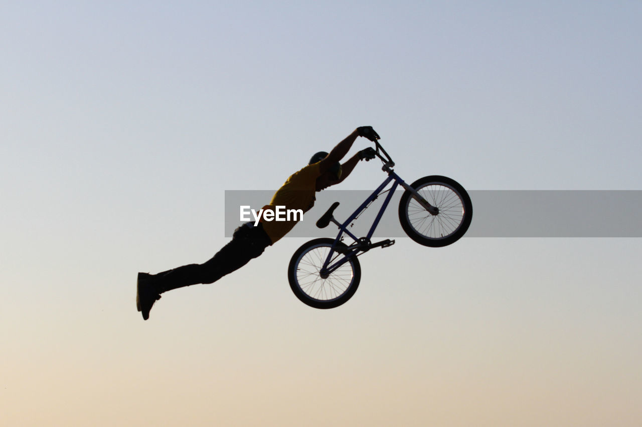 Man with bicycle jumping against clear sky
