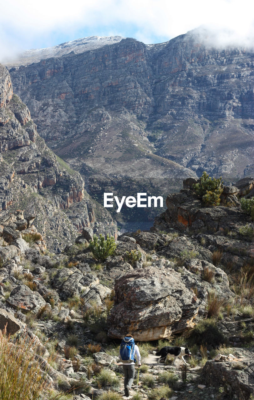 REAR VIEW OF WOMAN STANDING BY MOUNTAINS AGAINST SKY