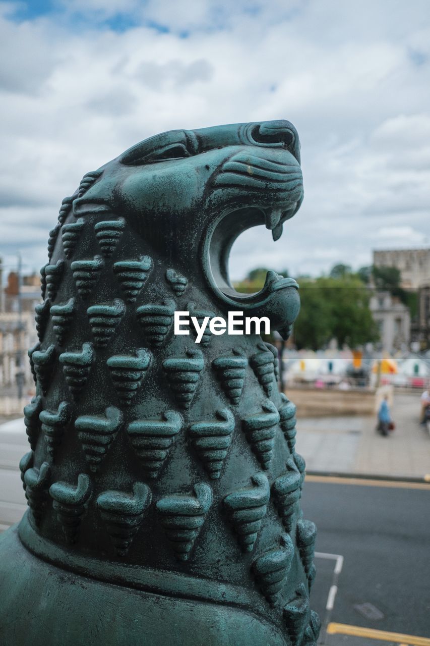 Gargoyle in city against cloudy sky