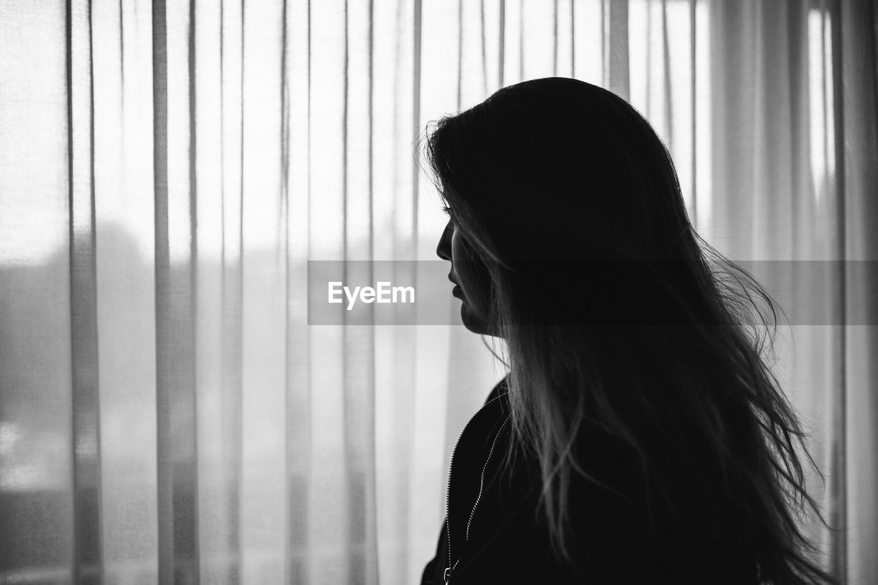Thoughtful woman looking through window at home