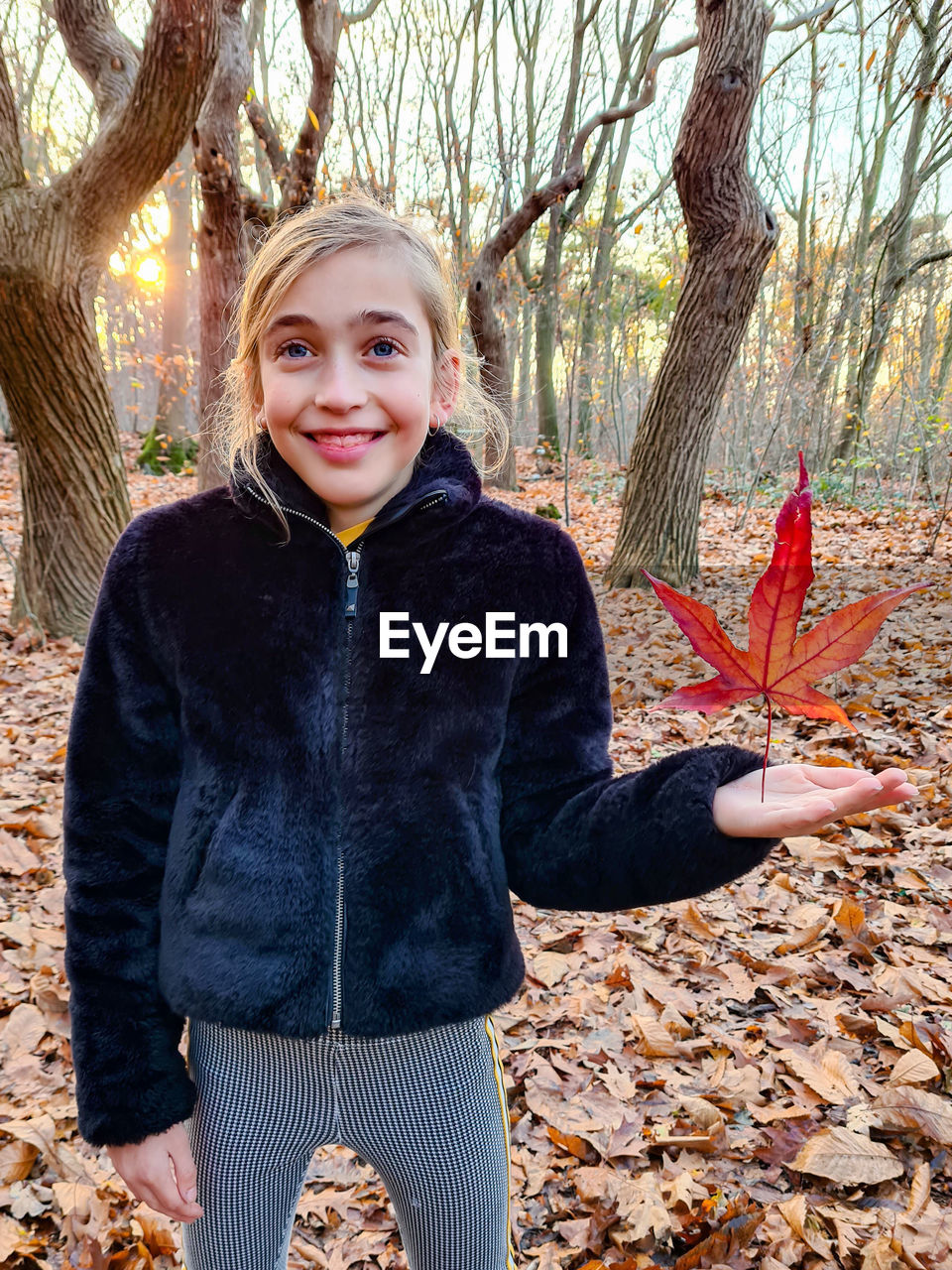 Portrait of a smiling girl in the forest holding a fallen autumn leaf 