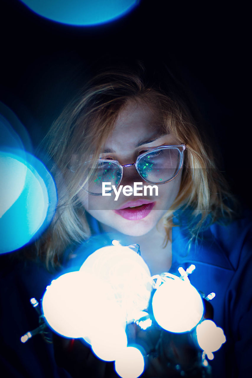 Close-up of young woman by illuminated lights in darkroom