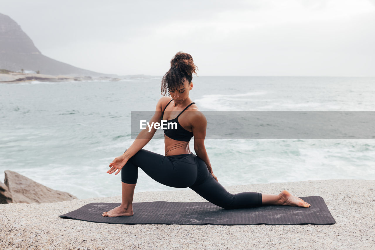 side view of woman sitting at beach against sky