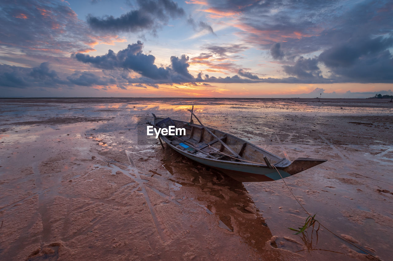 Boat moored on beach against sky during sunset