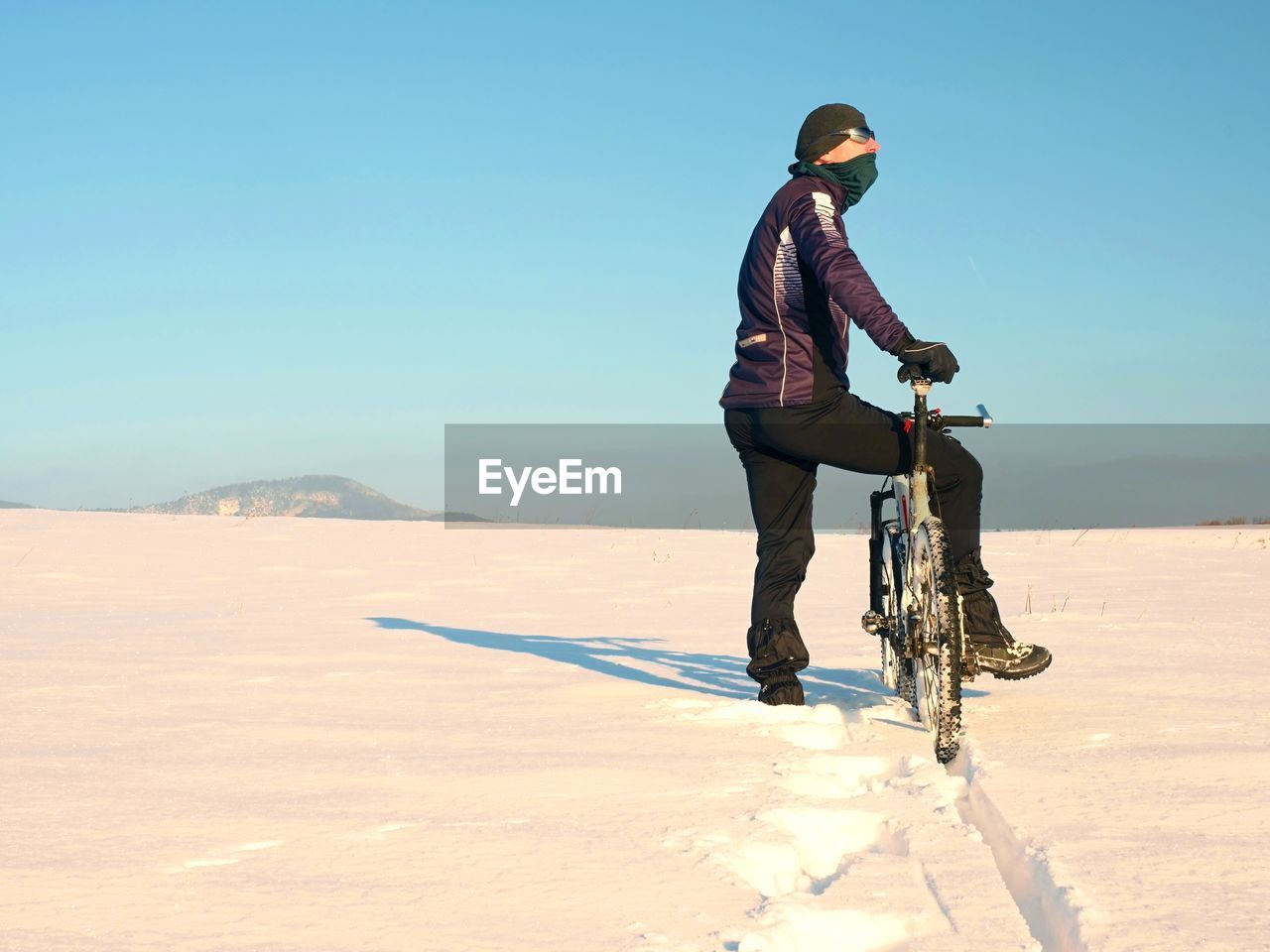 Biker pushing mountain bike on snow drift. freeze sunny winter weather. man sit on bike in deep snow