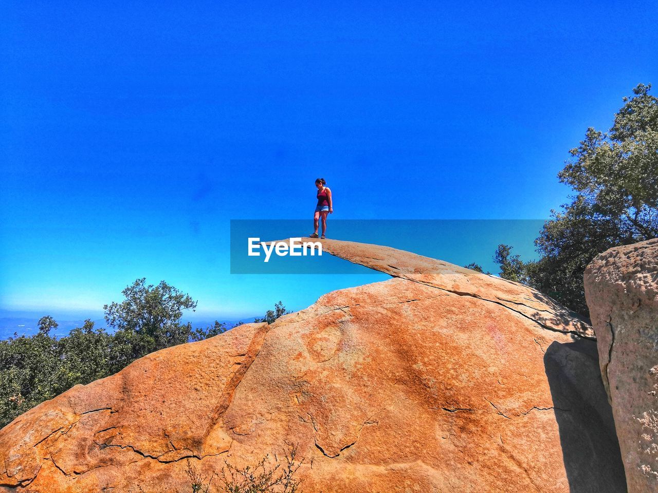 LOW ANGLE VIEW OF MAN ON ROCK AGAINST CLEAR SKY