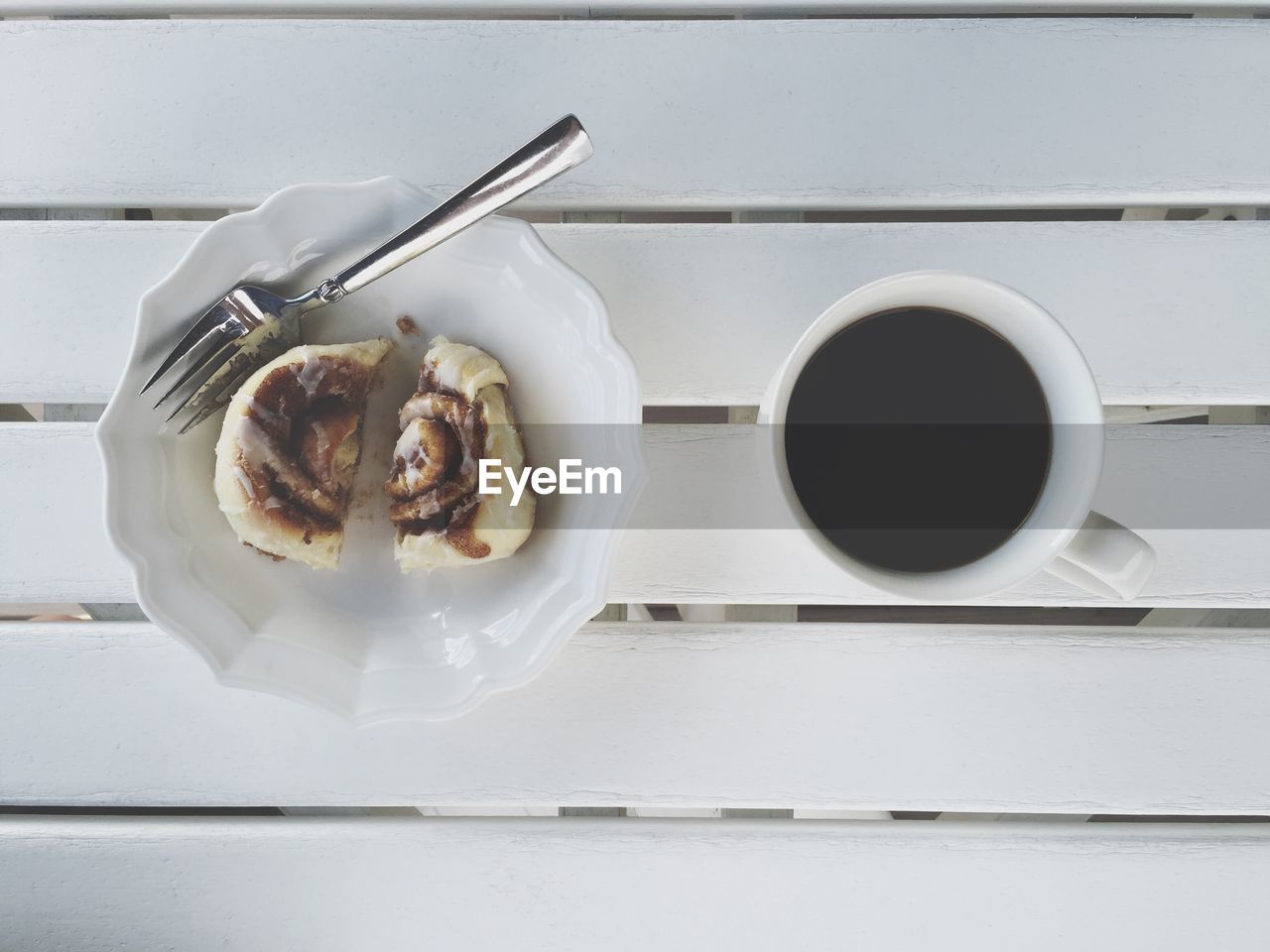 Directly above shot of cinnamon roll in bowl with black coffee on wooden table