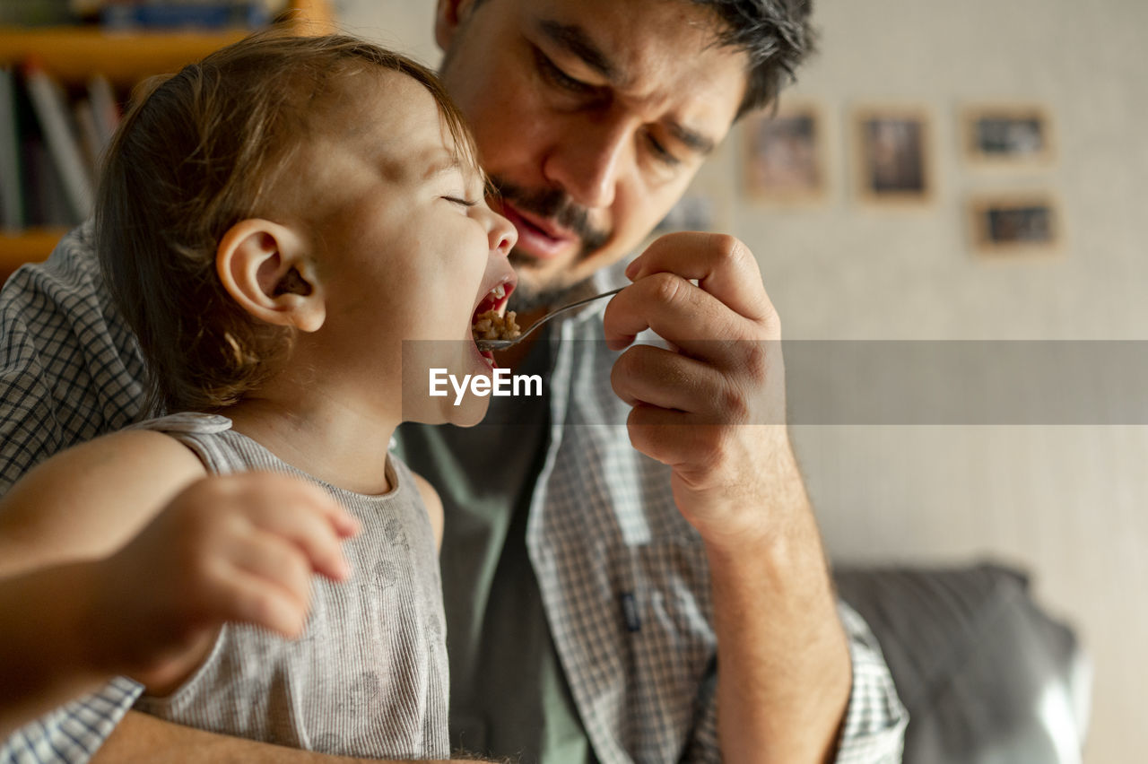 Father feeding porridge with spoon to son at home