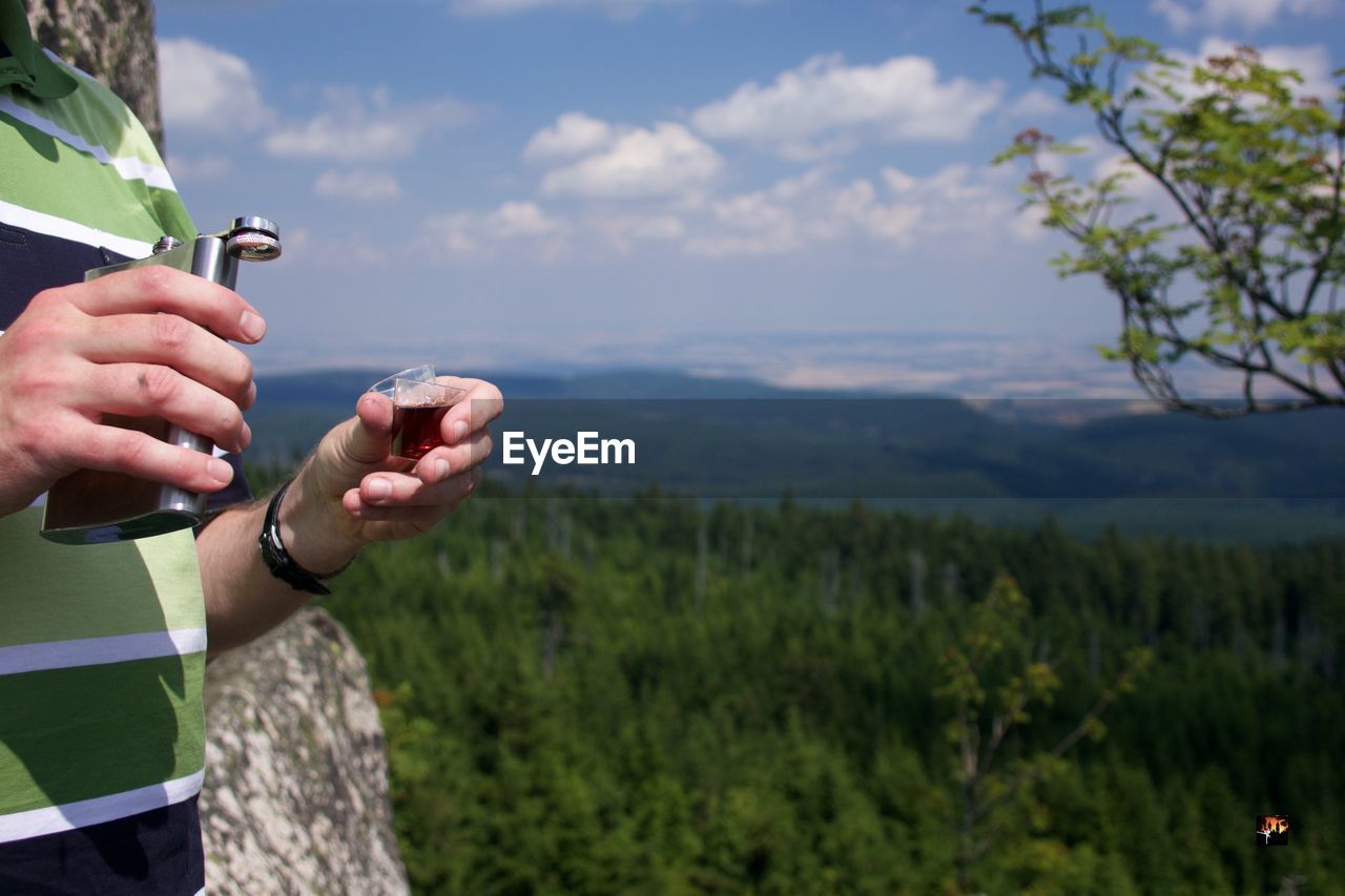 Midsection of man holding hip flask against mountain