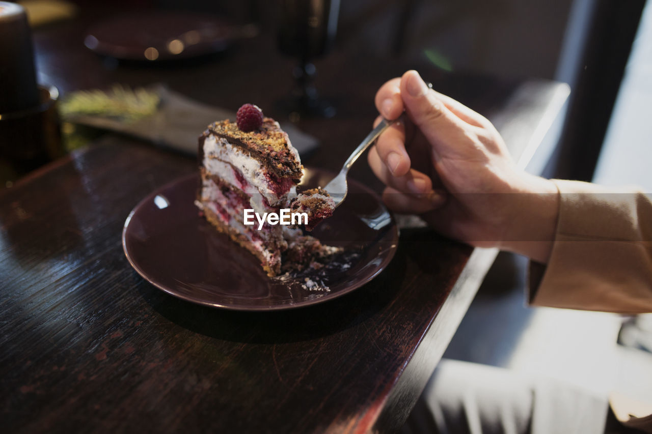 Cropped image of man eating cake slice at table