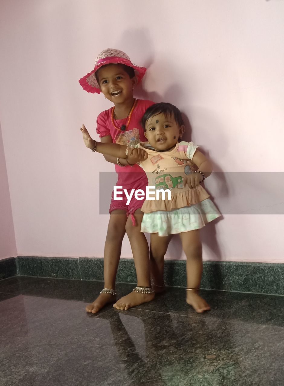 Cheerful sisters standing on floor against wall