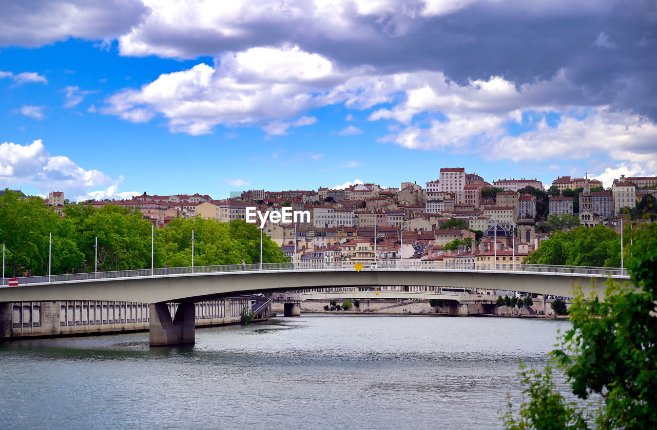 BRIDGE OVER RIVER AMIDST BUILDINGS AGAINST SKY