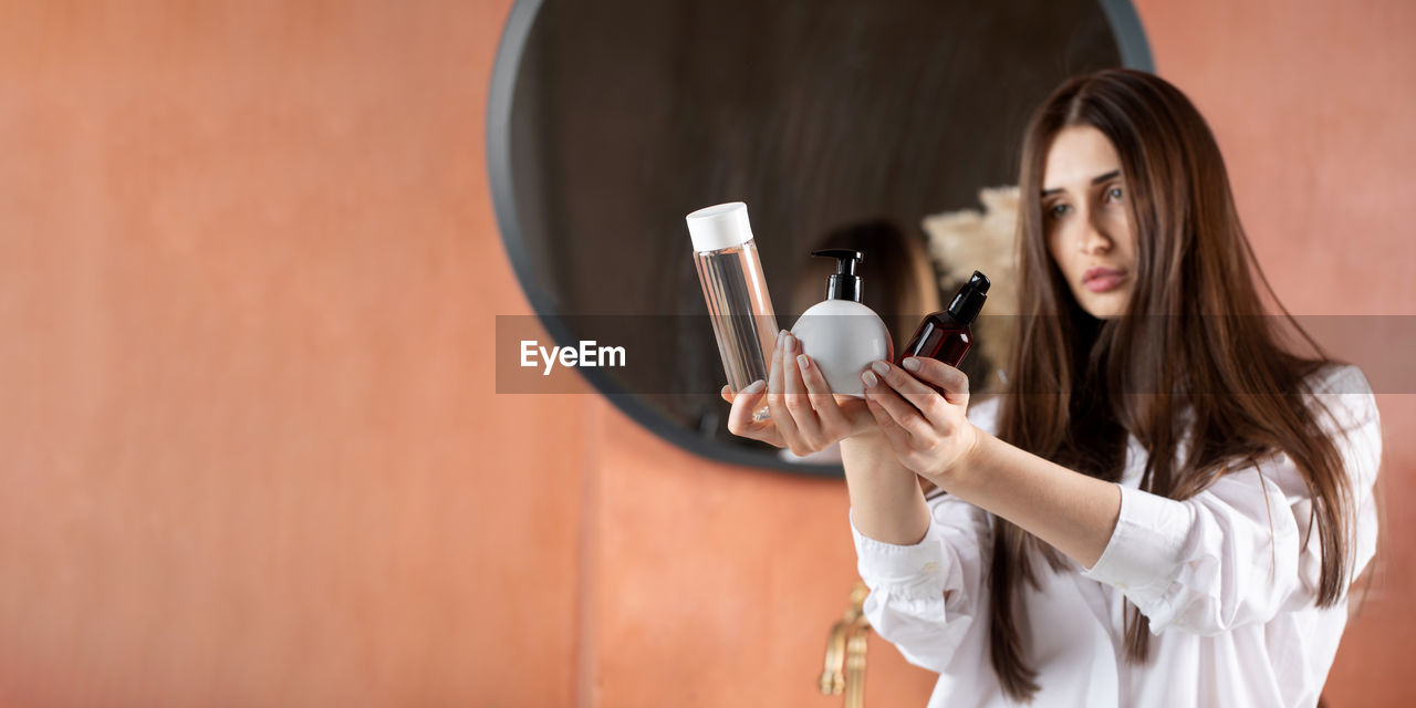 A beautiful brunette girl holds tubes of cosmetic products for hair and skin care. beauty concept. 