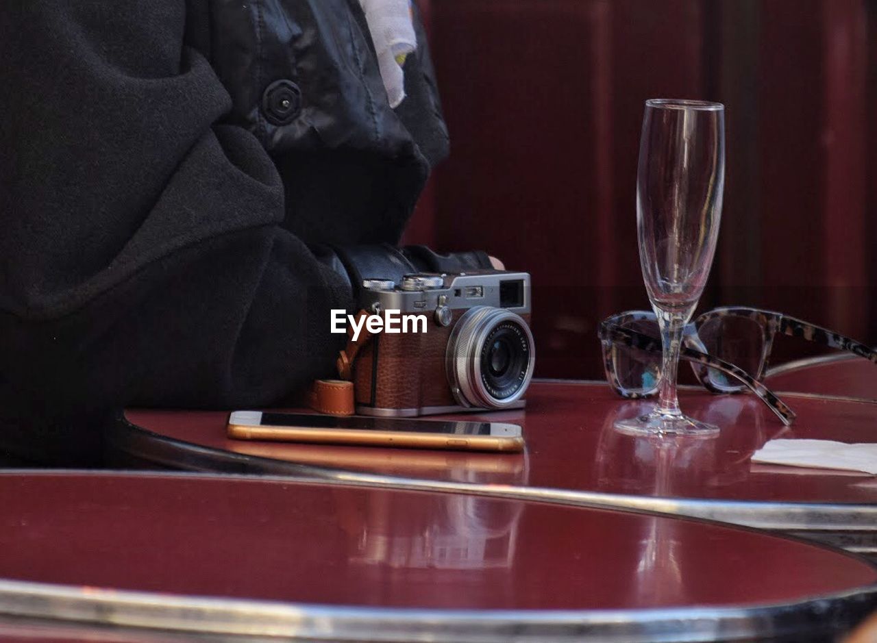 Midsection of person sitting by table with camera and smart phone