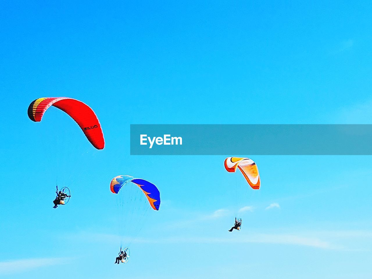 Low angle view of people paragliding against blue sky