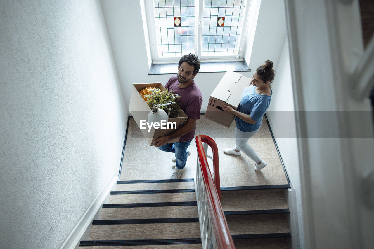 Smiling man and woman with cardboard boxes moving up on staircase