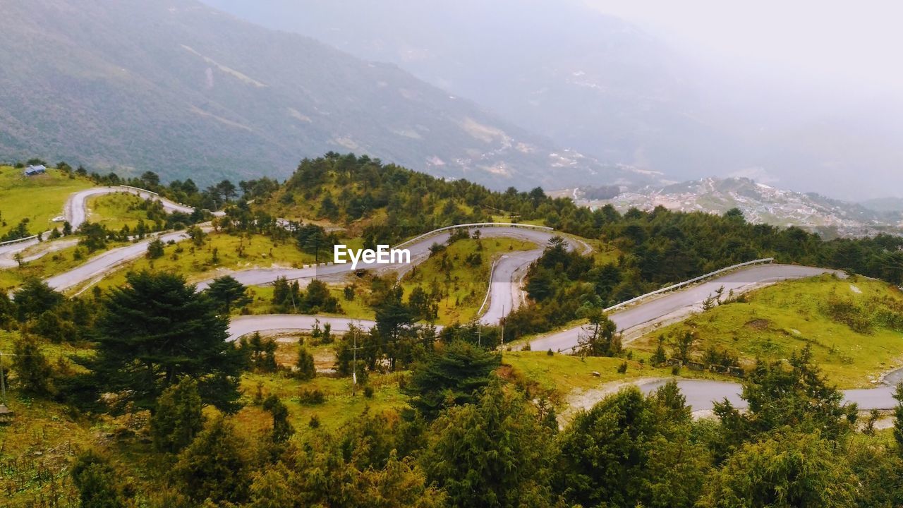 HIGH ANGLE VIEW OF ROAD AMIDST TREES AGAINST MOUNTAINS