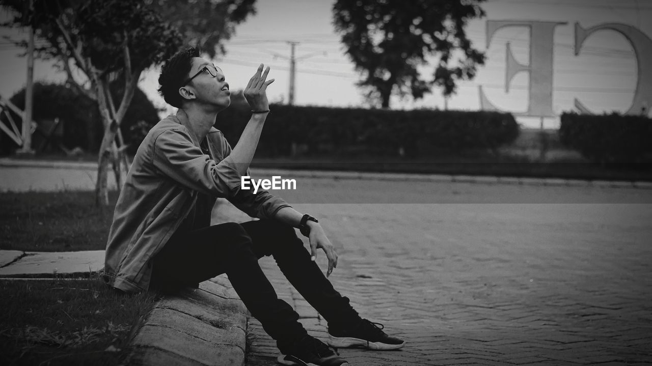 Side view of man looking away while sitting on tree