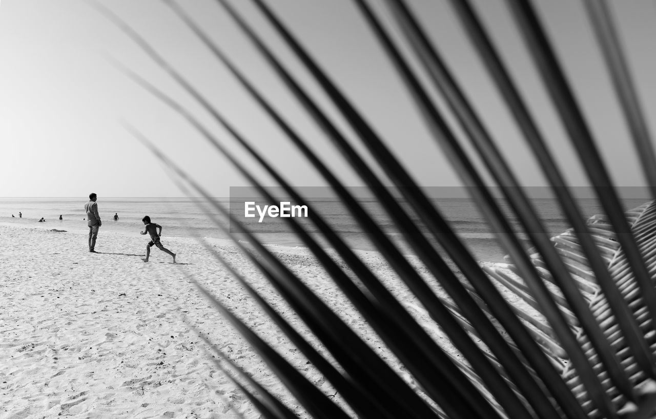 PEOPLE WALKING ON BEACH BY SEA