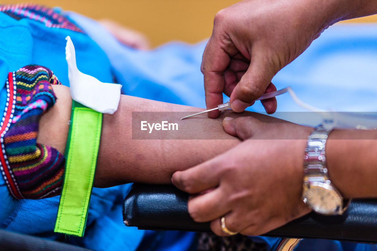 Cropped hand of male doctor injecting needle in patient hand on stretcher