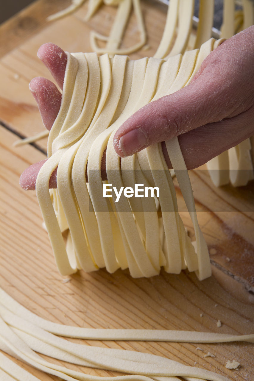 Cropped hand holding raw pasta on table