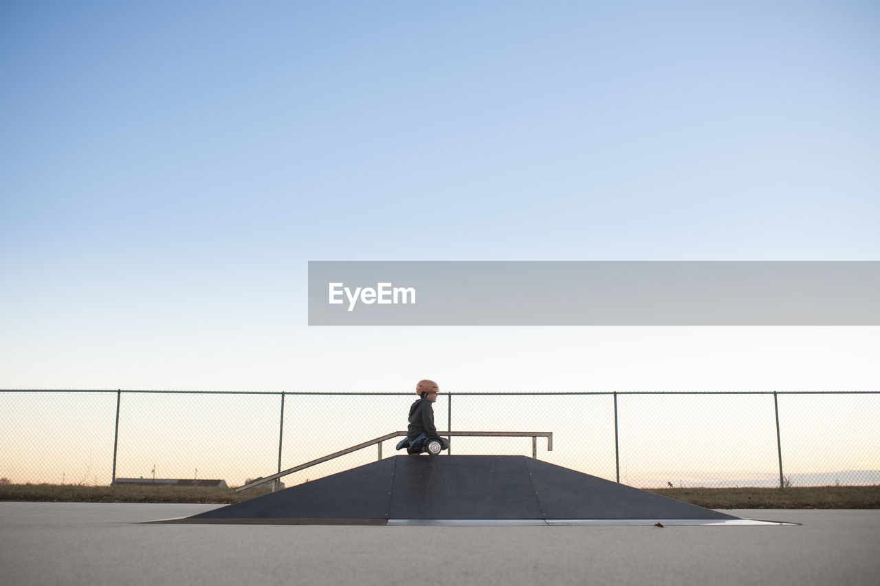 Young boy on top of ramp on hover board at skate park against blue sky