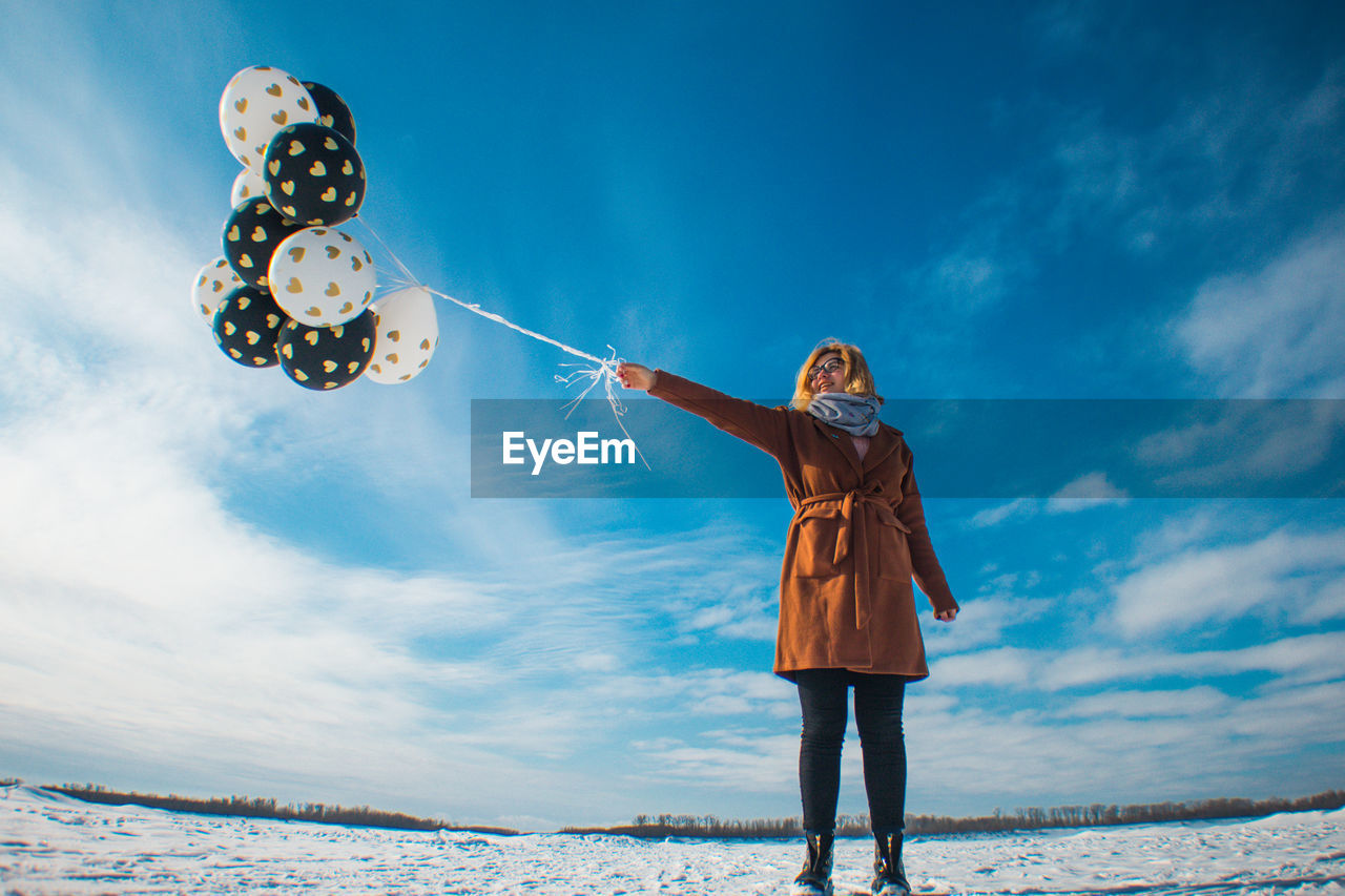 Woman with balloons standing on snow against sky