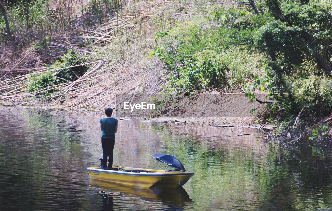 Rear view of man standing on boat floating on lake in forest