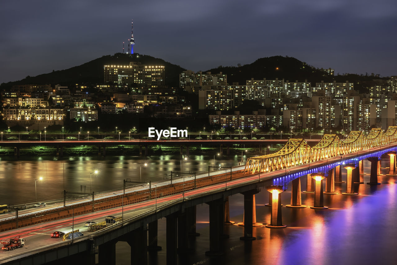 ILLUMINATED BRIDGE OVER RIVER AND BUILDINGS IN CITY AT NIGHT