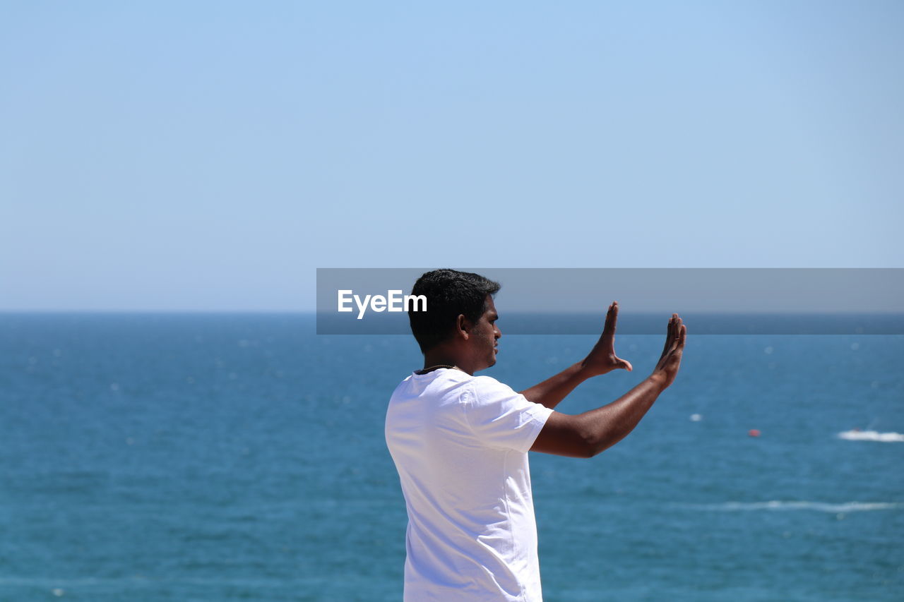 Rear view of mid adult man gesturing while standing at beach against sky