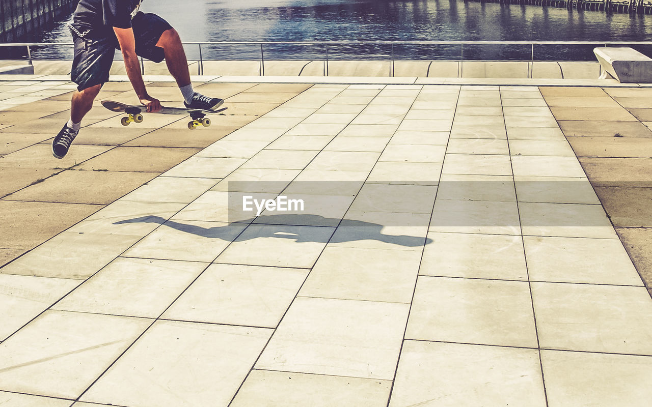 Low section of men skateboarding on sidewalk by canal