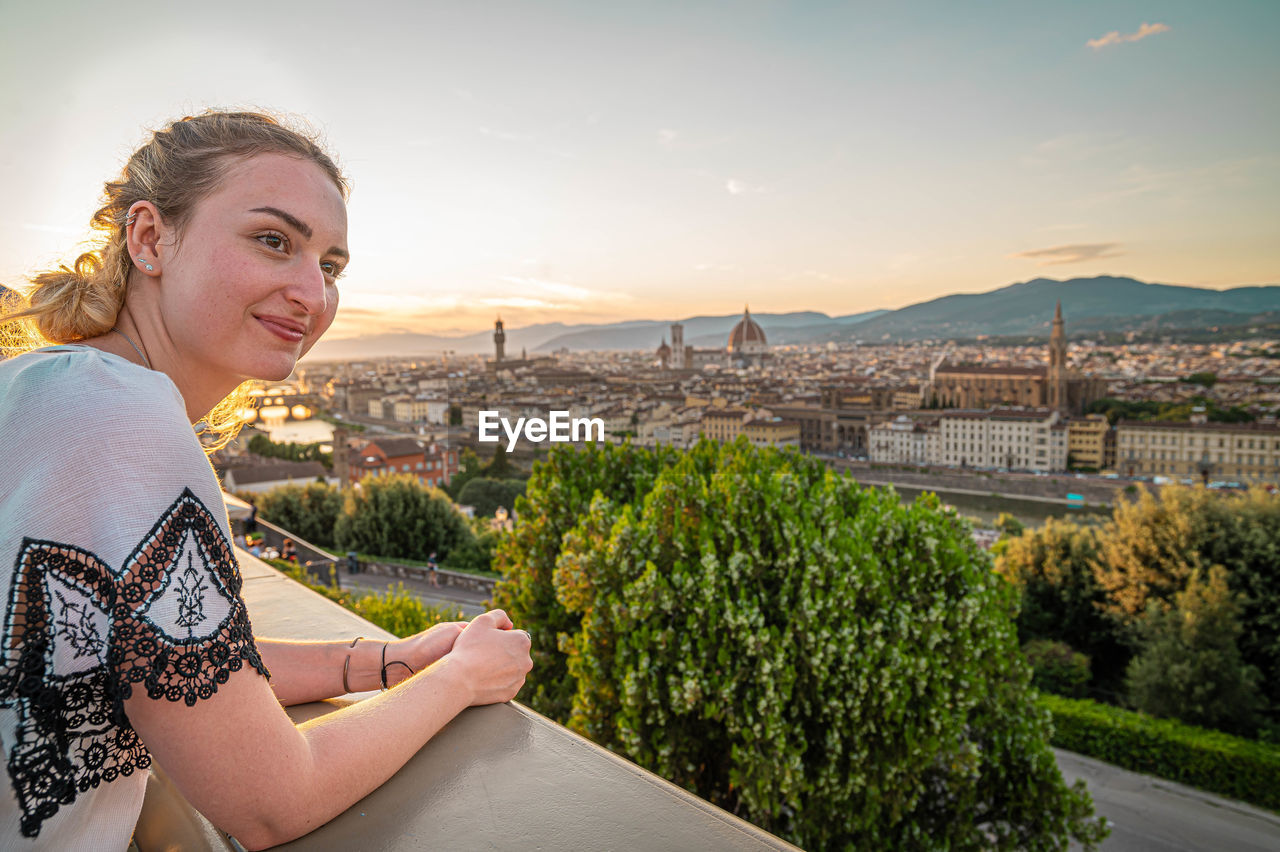 Woman in city against sky during sunset