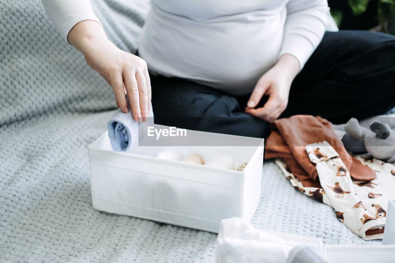 How to organize newborn baby clothes. pregnant woman using ornament boxes, baskets, or dividers to