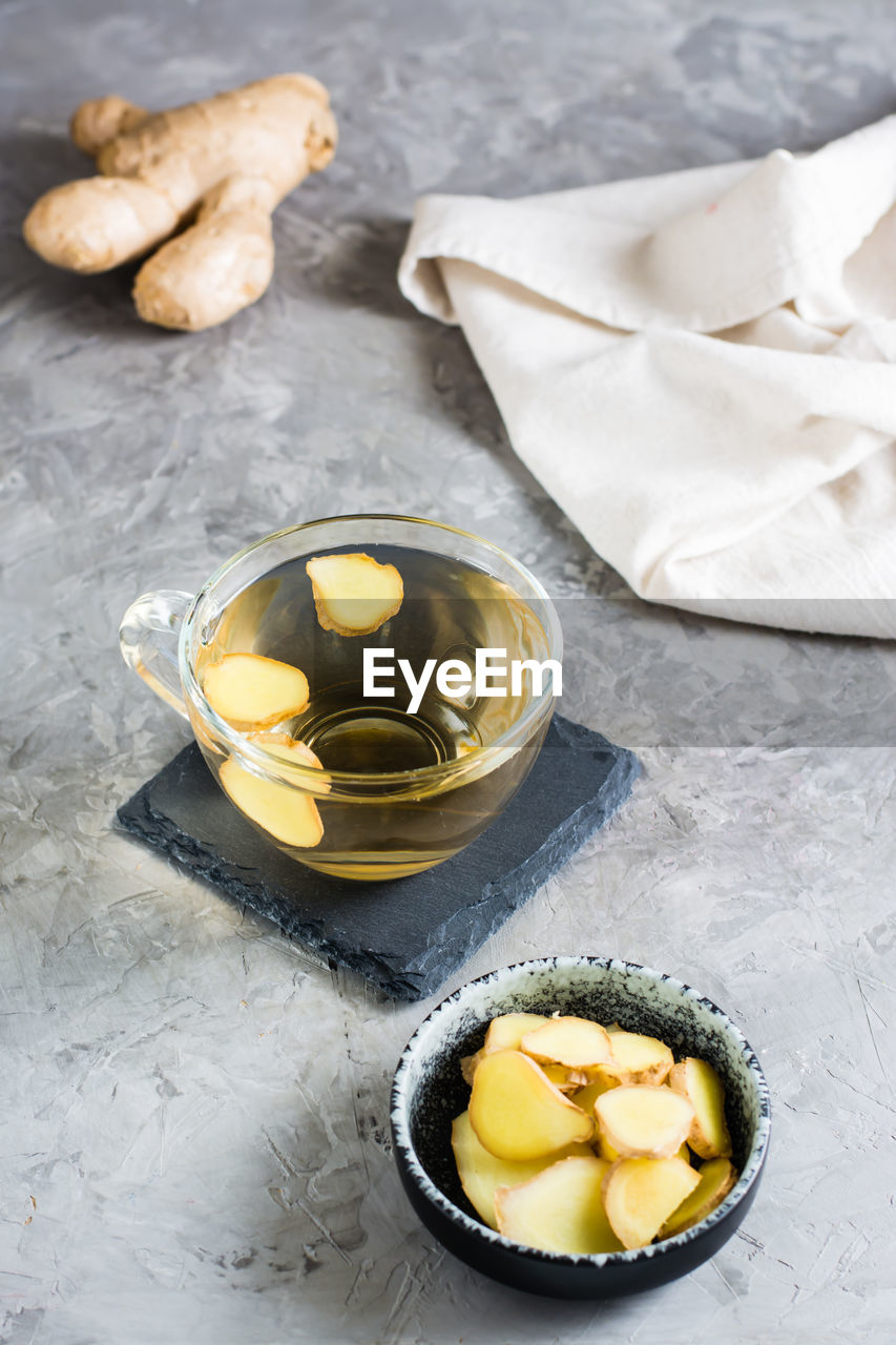 Ginger tea in a cup and chopped root in a bowl on the table. natural vitamins. vertical view