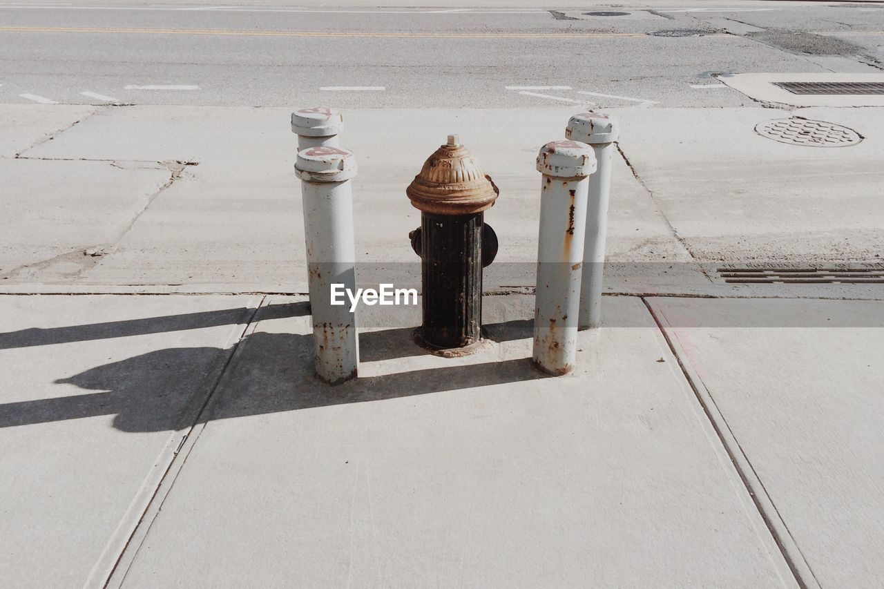 High angle view of fire hydrant amidst rusty metallic bollards on sidewalk