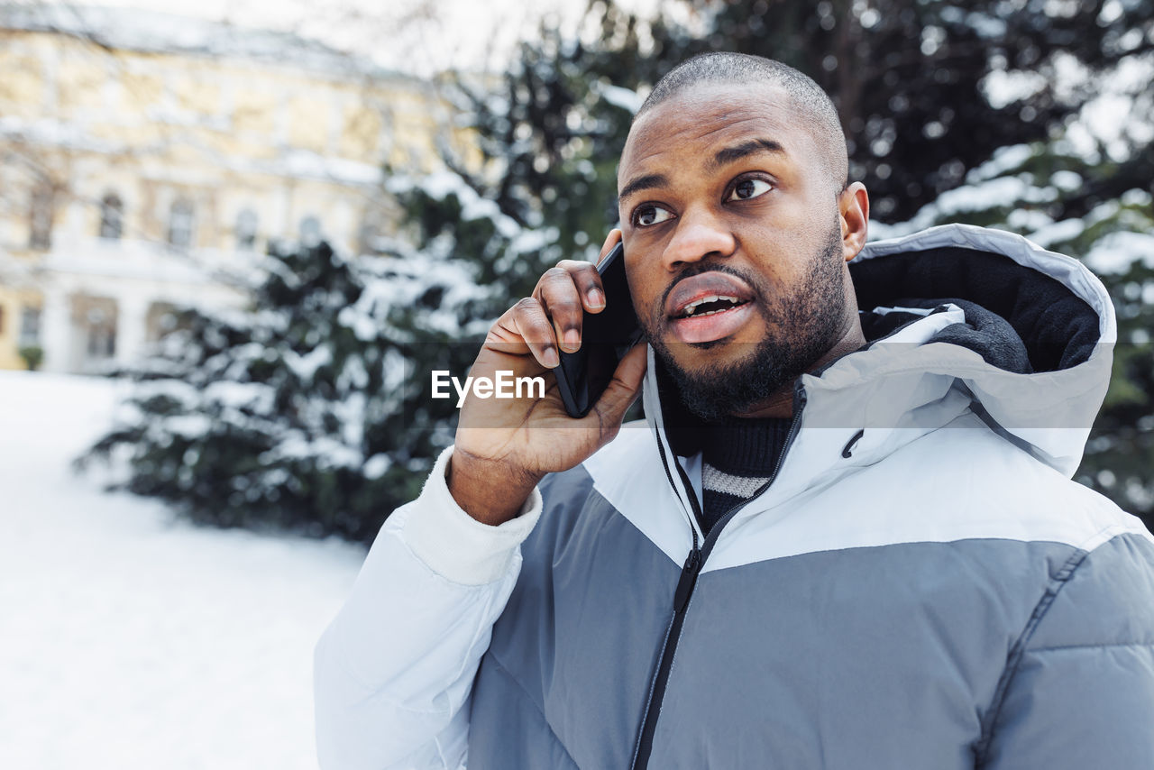 Young african man man talking on phone shocked, winter outdoor