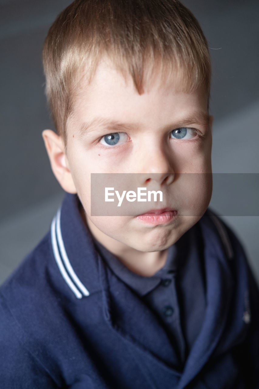 Portrait of a 6 year old boy with blond hair and blue eyes , with a serious expression on his face