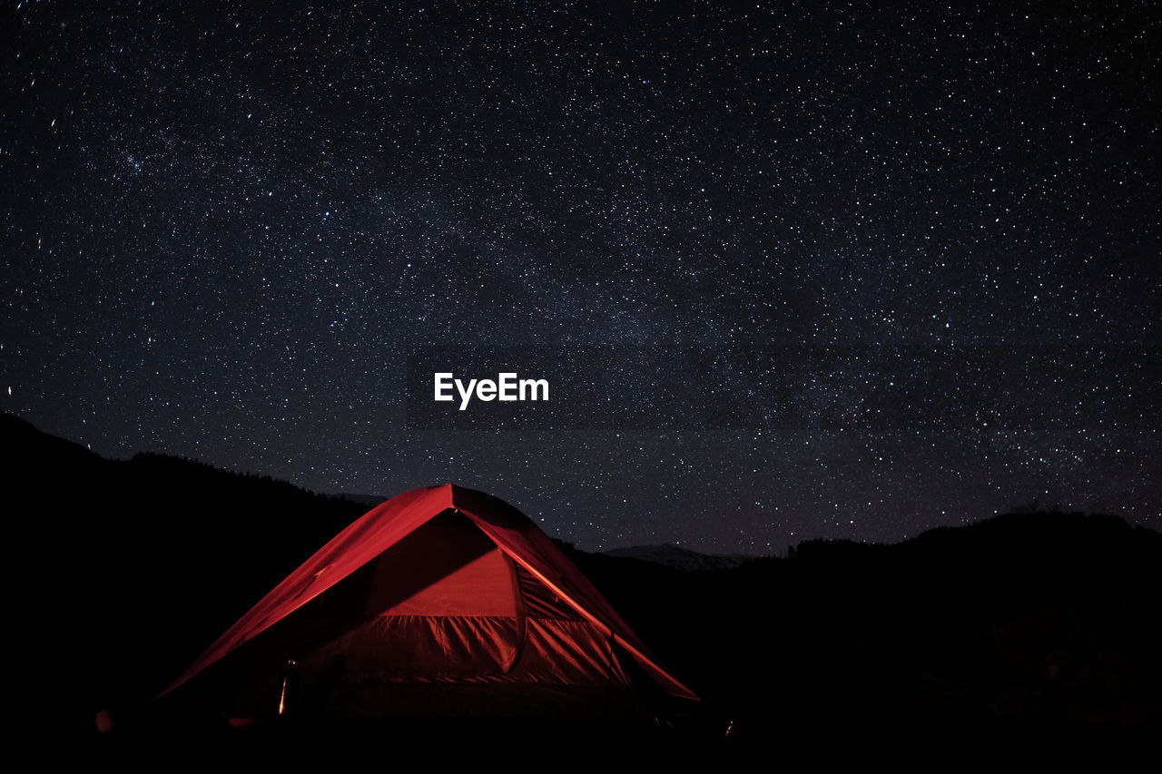 Tent and silhouette mountains against star field at night