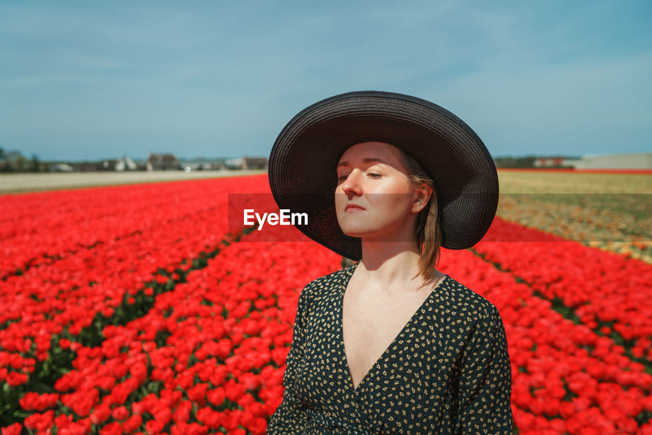 Mid adult woman wearing hat standing against red plants